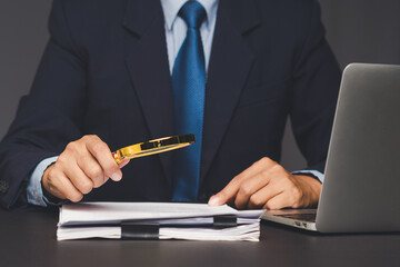 Businessman analyzing document with magnifying glass at office desk.