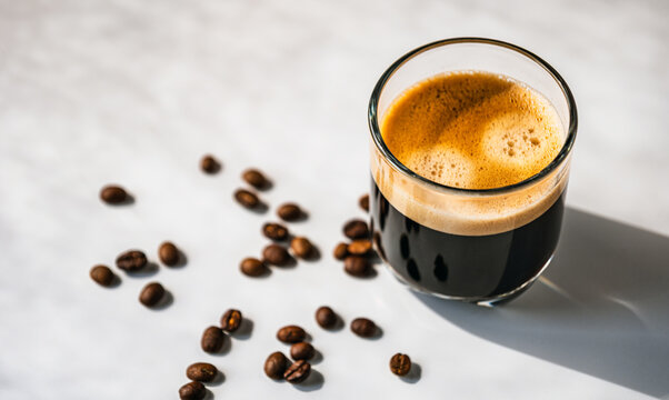 Hot espresso coffee steam rises from hot coffee in coffee glass and bean isolated on white background in Morning sunlight