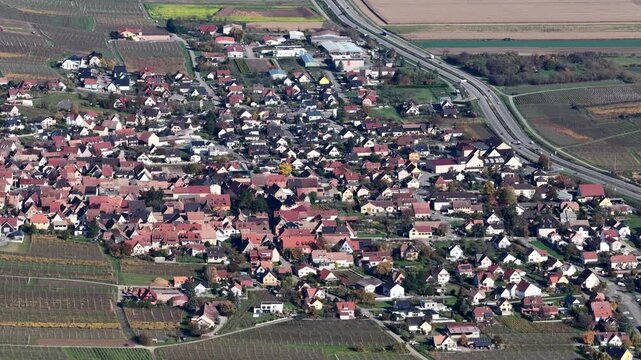 Aerial view of the sprawling cityscape of Rouffach with its red-roofed buildings nestled among vineyards and adjacent to a highway, Rouffach, Grand Est, France.