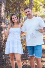 Naklejka premium Pregnant couple holding baby name letters outdoors in sunny nature. Future parents smiling with happiness and tenderness, celebrating pregnancy and family love in warm bright light.Vertical