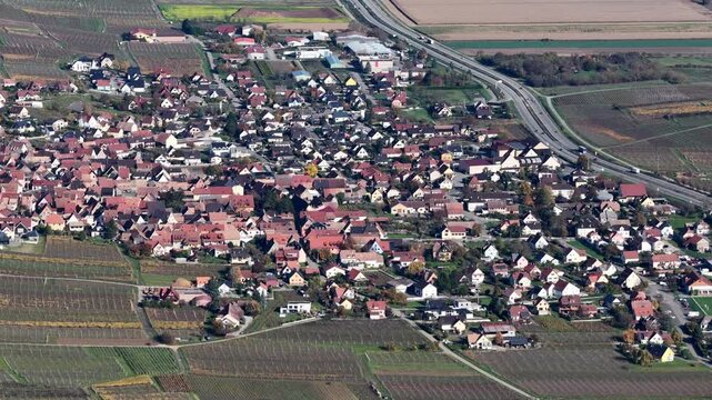 Aerial view of a town with red-roofed buildings nestled among vineyards, bordered by a highway and fields, creating a blend of rural and urban landscapes, Rouffach, Grand Est, France.