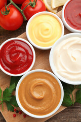 Different sauces in bowls and ingredients on wooden table, flat lay