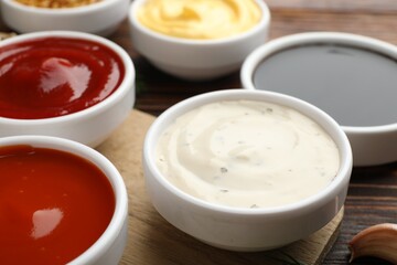 Different sauces in bowls on wooden table, closeup