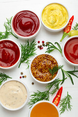 Different sauces in bowls and ingredients on white wooden table, flat lay