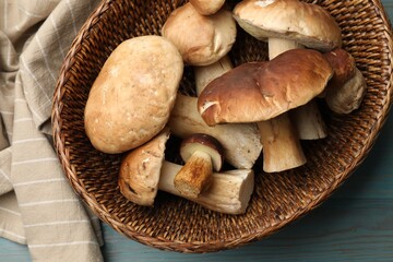 Fresh porcini mushrooms in wicker basket on light blue wooden table, top view