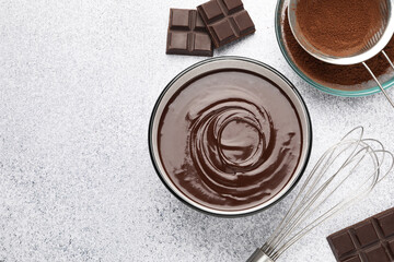 Melted chocolate in bowl, pieces, cocoa powder and whisk on light grey table, flat lay. Space for...