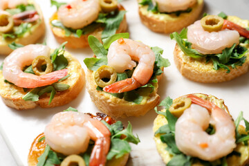 Delicious bruschettas with shrimps, olives and arugula on light table, closeup