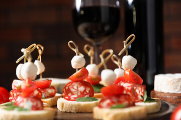 Delicious bruschettas with salami, mozzarella and tomatoes served with red wine on table, closeup