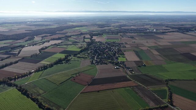 Aerial view of agricultural fields in varied shades of green and brown, creating a patchwork quilt effect, divided by roads and waterways, Rouffach, Grand Est, France.