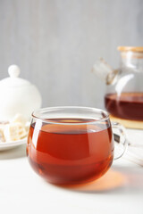 Tasty tea in glass cup on white table against grey background, closeup