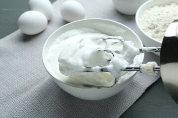 Whipped whites in bowl, mixer, flour and eggs on grey wooden table, closeup
