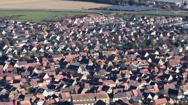 Aerial view of the tightly packed rooftops with varying shades of red and brown surrounding a church in a dense town, Rouffach, Grand Est, France.