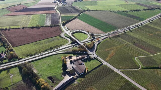 Aerial view of a roundabout intersecting roads, surrounded by fields with diverse textures and colors, creating a structured landscape, Rouffach, Grand Est, France.