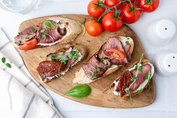 Delicious bruschettas with roast beef served on white table, flat lay