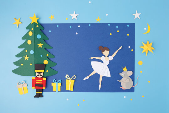 Paper cut composition with ballerina, nutcracker soldier, mouse king, Christmas tree, stars, and gifts on blue background. Handmade craft art in flat lay copy space. Christmas winter holiday concept
