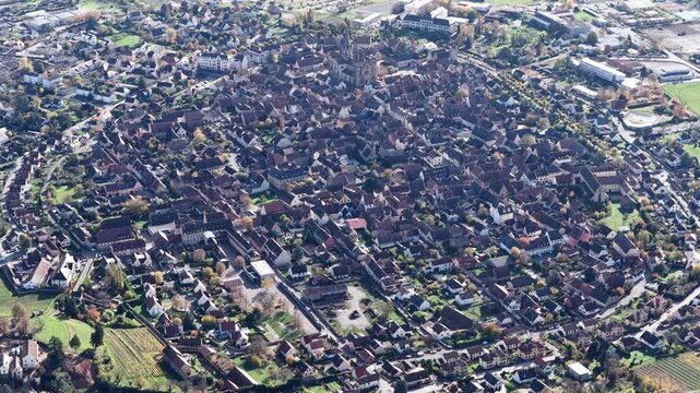 Aerial view of Rouffach, a tapestry of red-roofed buildings nestled amidst the green and brown hues of surrounding fields, Rouffach, Grand Est, France.