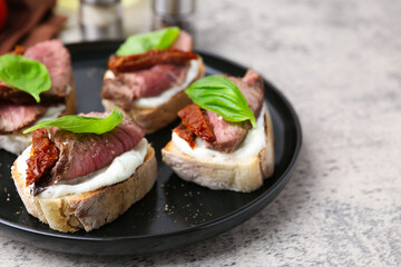 Bruschettas with roast beef, cream cheese, basil and sun-dried tomato on grey table, closeup. Space for text