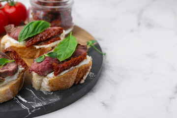 Bruschettas with roast beef, cream cheese, basil, sun-dried tomatoes and fresh vegetables on white marble table, closeup. Space for text