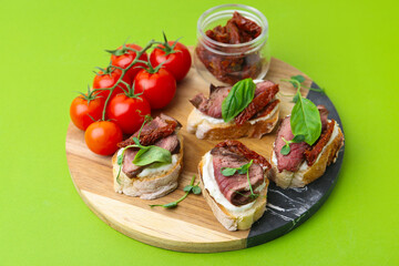 Bruschettas with roast beef, cream cheese, basil, sun-dried tomatoes and fresh vegetables on green background, closeup
