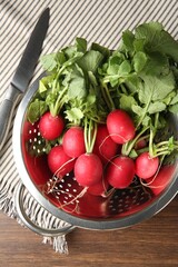Fresh ripe radishes in colander and knife on wooden table, top view