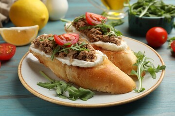 Delicious bruschettas with tuna, cream cheese and tomatoes on light blue wooden table, closeup