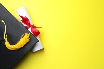 Diploma and graduation hat on yellow background, top view. Space for text
