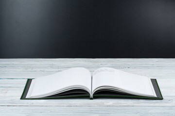 Open book on wooden deck table and black board background. Back to School. Education concept with copy space for your ad text.