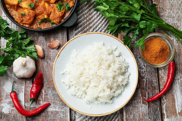 Chicken tikka masala with rice and spices on wooden table, flat lay