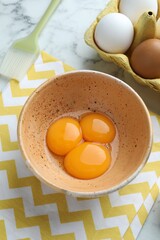 Raw eggs, yolks and brush on white marble table, above view