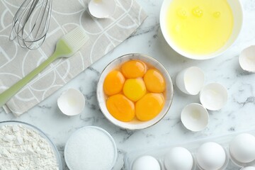 Raw eggs, yolks, other ingredients, brush and whisk on white marble table, flat lay