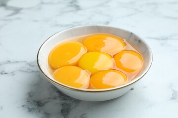 Egg yolks in bowl on white marble table, closeup