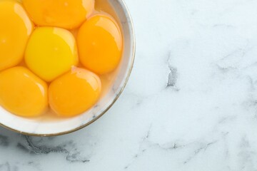 Egg yolks in bowl on white marble table, top view. Space for text