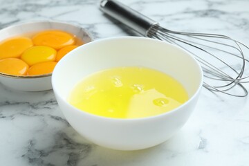 Egg whites, yolks and whisk on white marble table, closeup