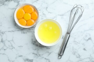 Egg whites, yolks and whisk on white marble table, flat lay