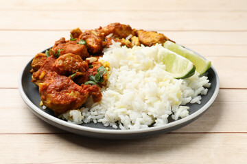 Delicious chicken tikka masala with rice, parsley and lime on light wooden table, closeup