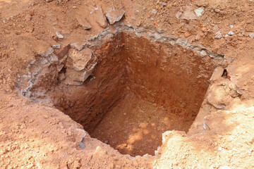 Obraz premium Deep square hole set in clay soil, ready for construction backfill or foundational support, ideal for civil engineering, housing development, and earthwork themes.