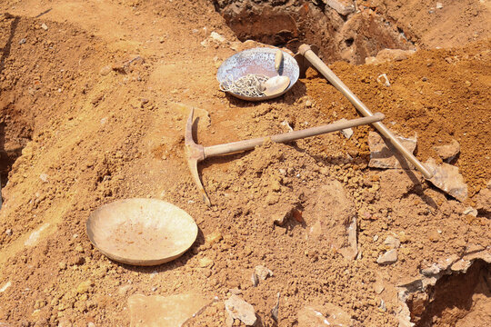 Indian site tools for excavation—pickaxe and sand plates—on reddish dirt, showing essential hand tools for home building or civil engineering work.