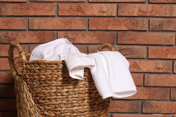 Wicker basket full of laundry near brick wall, closeup. Space for text