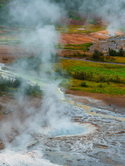 Billowing steam rises from bubbling Geysir at Haukadalur, Iceland, with winding runoffs, rust...