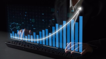 A business professional interacts with a keyboard while overseeing a digital graph, illustrating...
