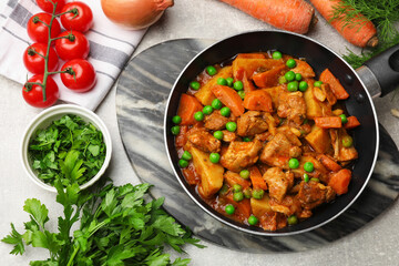 Delicious cooked stew in frying pan and ingredients on grey table, flat lay