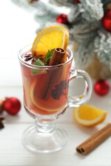 Tasty punch drink in glass, spices and Christmas decor on white wooden table, closeup