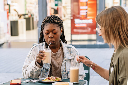 Multiethnic women couple enjoying coffee and brunch outdoors
