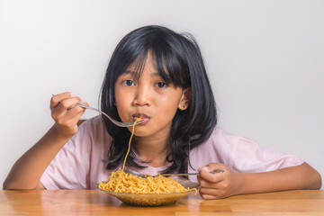 A beautiful little Asian girl eating fried noodles with a fork
