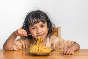 A cute little Asian girl holding a fork while eating fried noodles