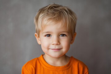 Fototapeta premium a cute 4-year-old boy with light blonde hair, wearing an orange t-shirt, soft smile, natural lighting, light gray studio background