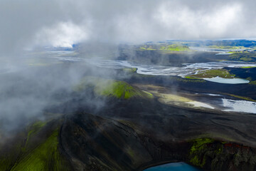 Braided glacial rivers wind over dark volcanic sands in Iceland near Landmannalaugar. Crater rims, tephra fields, and turquoise pools appear in soft, diffused light.