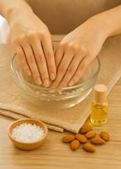 Close-up of woman soaking hands in warm water with sea salt and almond oil. Natural spa manicure treatment for soft skin and healthy nails. Beauty, wellness, and hand care concept.