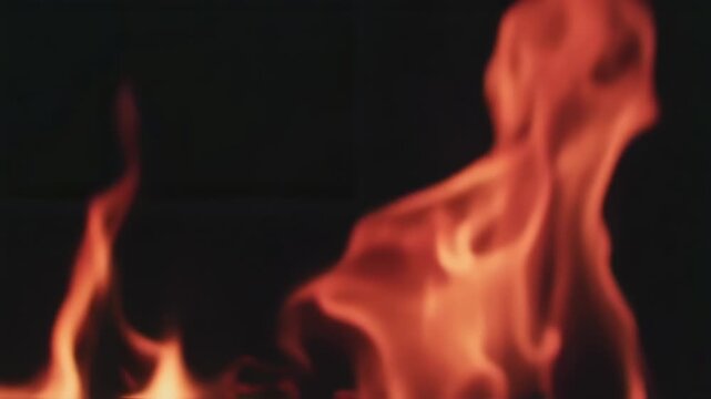 Blurred close-up view of vibrant orange flames against a dark, undefined background. The fire seems to be alive