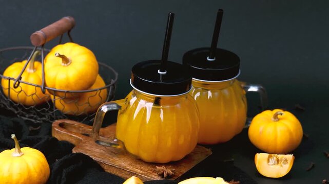 Orange pumpkin juice in jars with straws, mini pumpkins, cloves and spices on dark